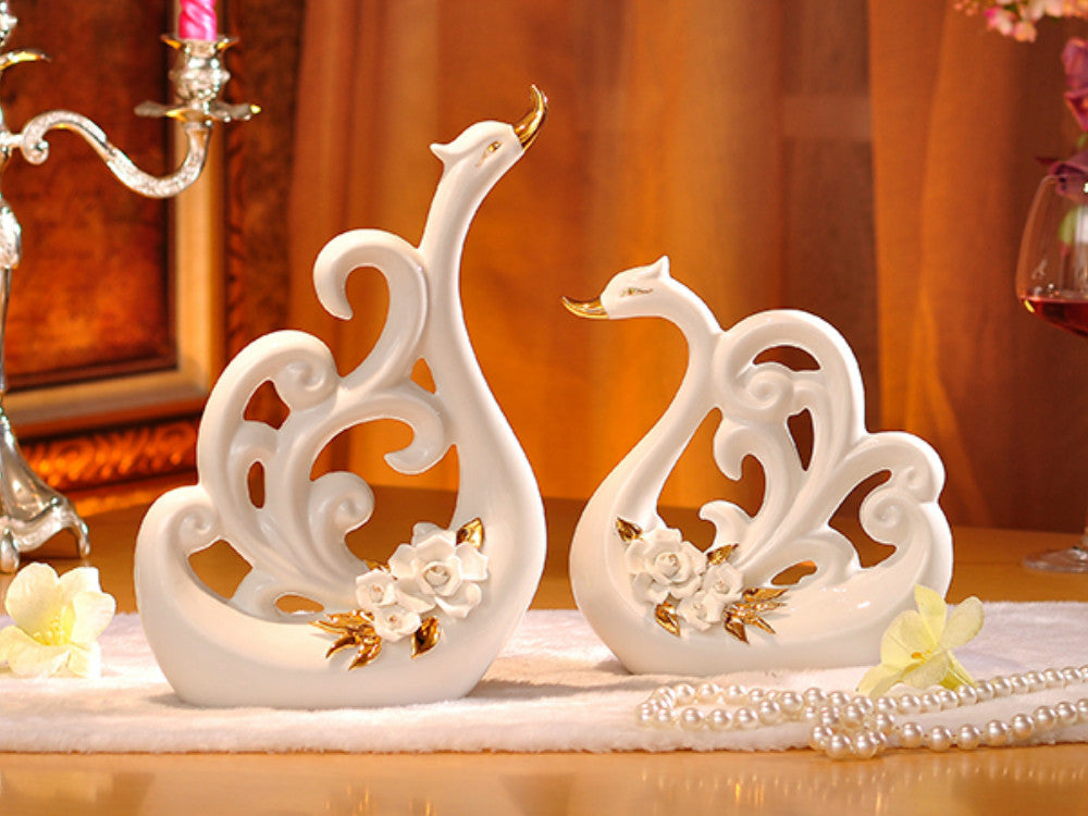Pair of white porcelain swans with decorative wings for table decor.