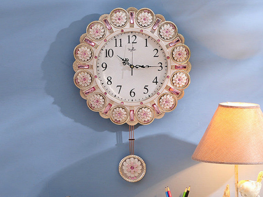 Metallic gold wall clock with pendulum and pink stone accents.